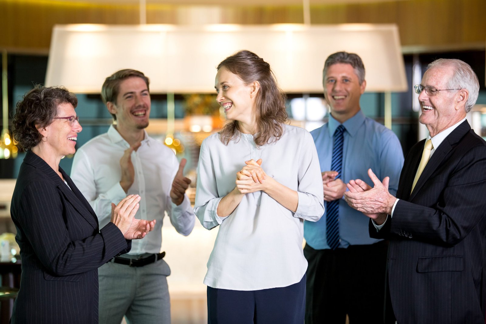 Closeup of four smiling people applauding and congratulating business woman and standing around her with blurred view in background.