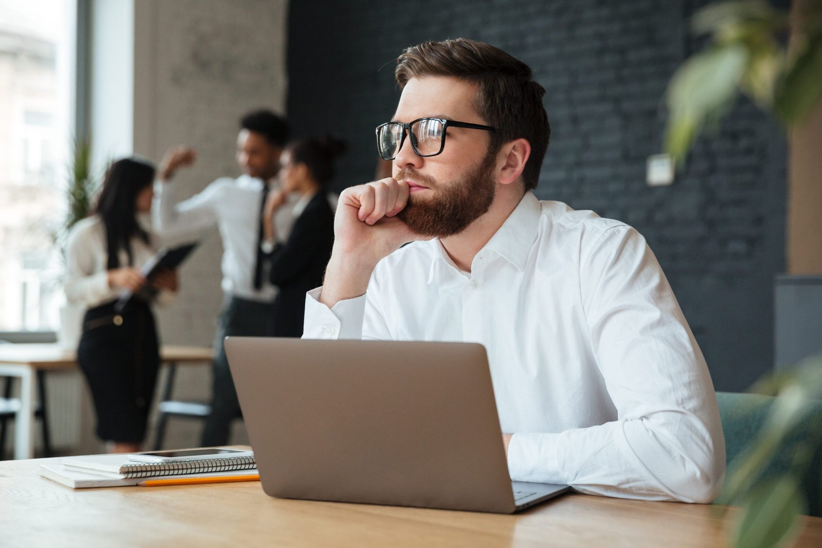Image of concentrated young caucasian businessman sitting indoors using laptop computer. Looking aside.