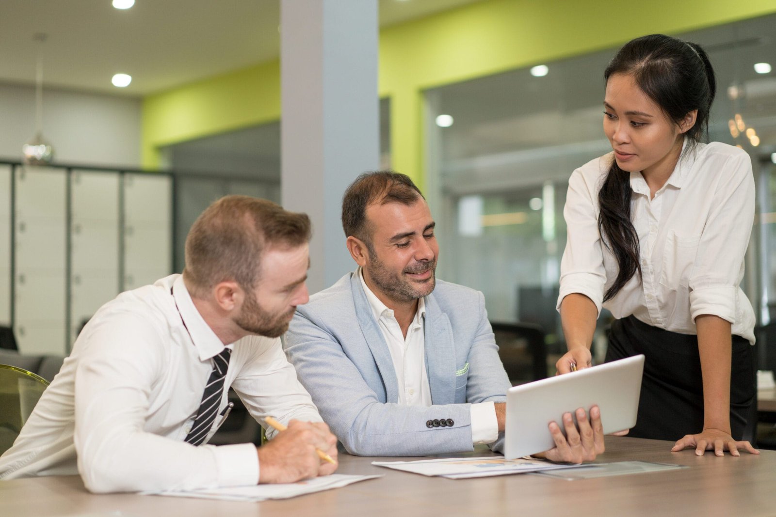 Asian business lady working with coworkers at desk in office. Businesspeople discussing issues, using tablet computer and sitting at desk. Modern office work concept.