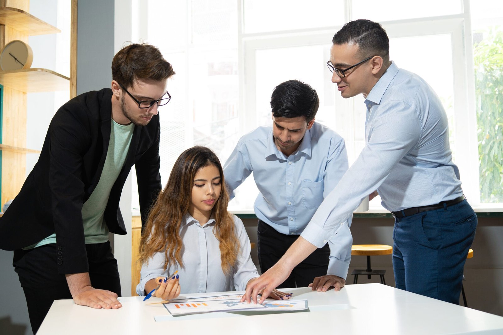 Mentor explaining marketing data interns. Confident office worker showing diagram to three pensive and focused colleagues. Mentorship concept