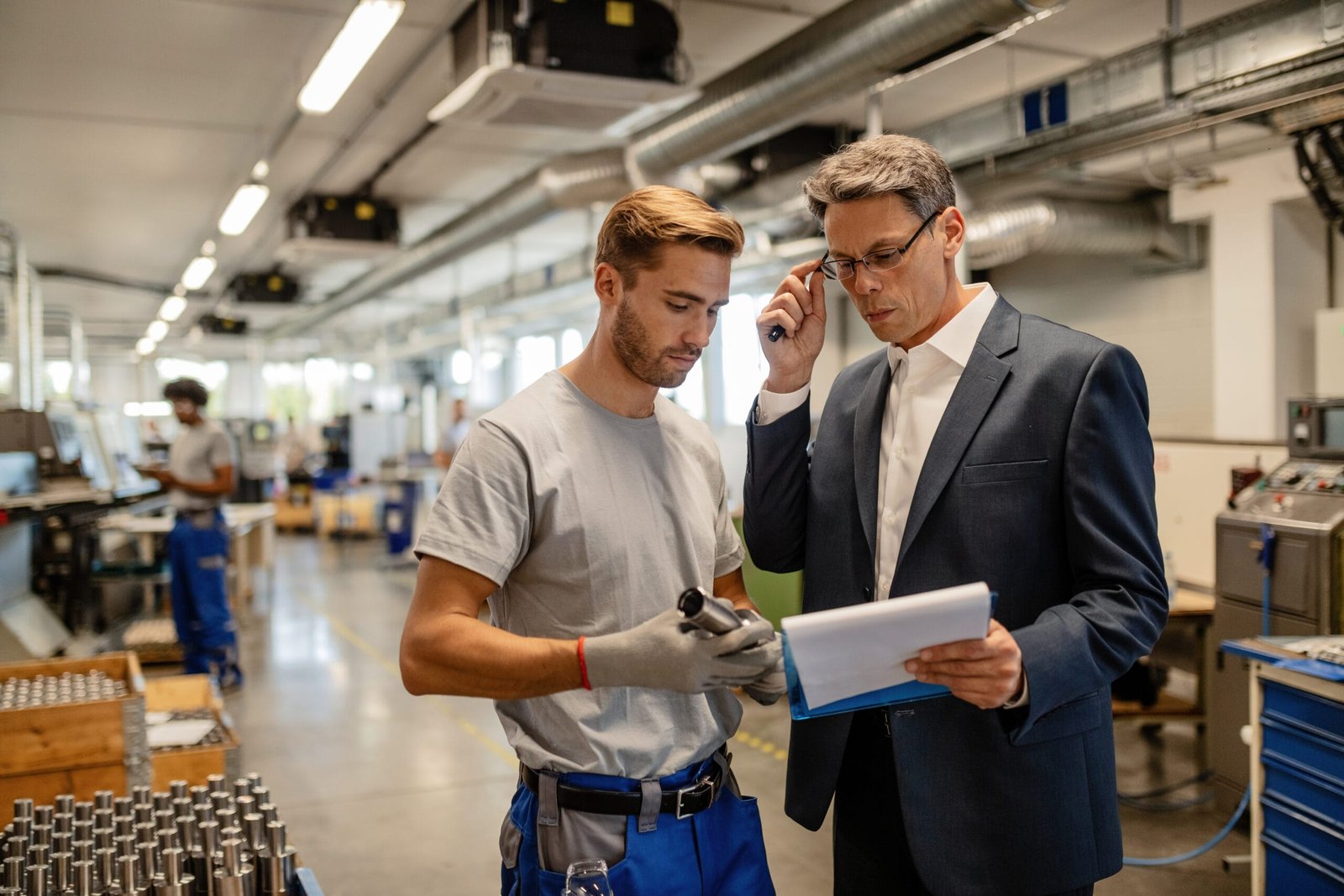 Mid adult engineer and young worker cooperating while analyzing reports in steel factory.