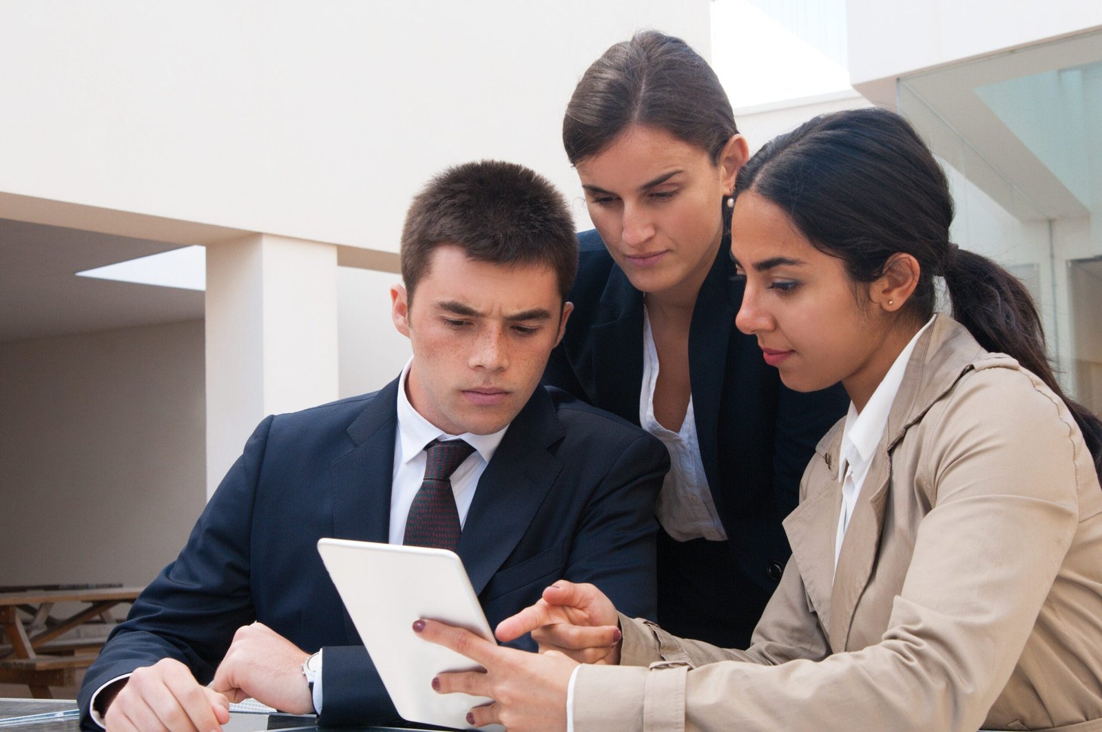 Serious woman showing tablet screen to business people. Business man and women discussing issues, standing and sitting at cafe table. Order concept. Front view.