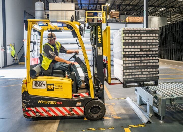 A warehouse worker maneuvers a forklift to transport crates for brewing company storage