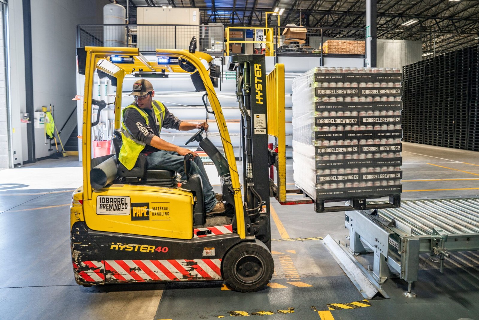 A warehouse worker maneuvers a forklift to transport crates for brewing company storage