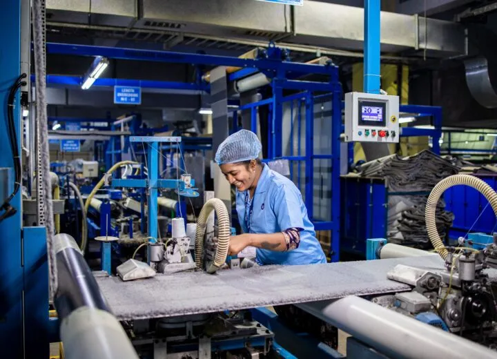 Female factory worker smiling while operating complex textile machinery in an industrial setting
