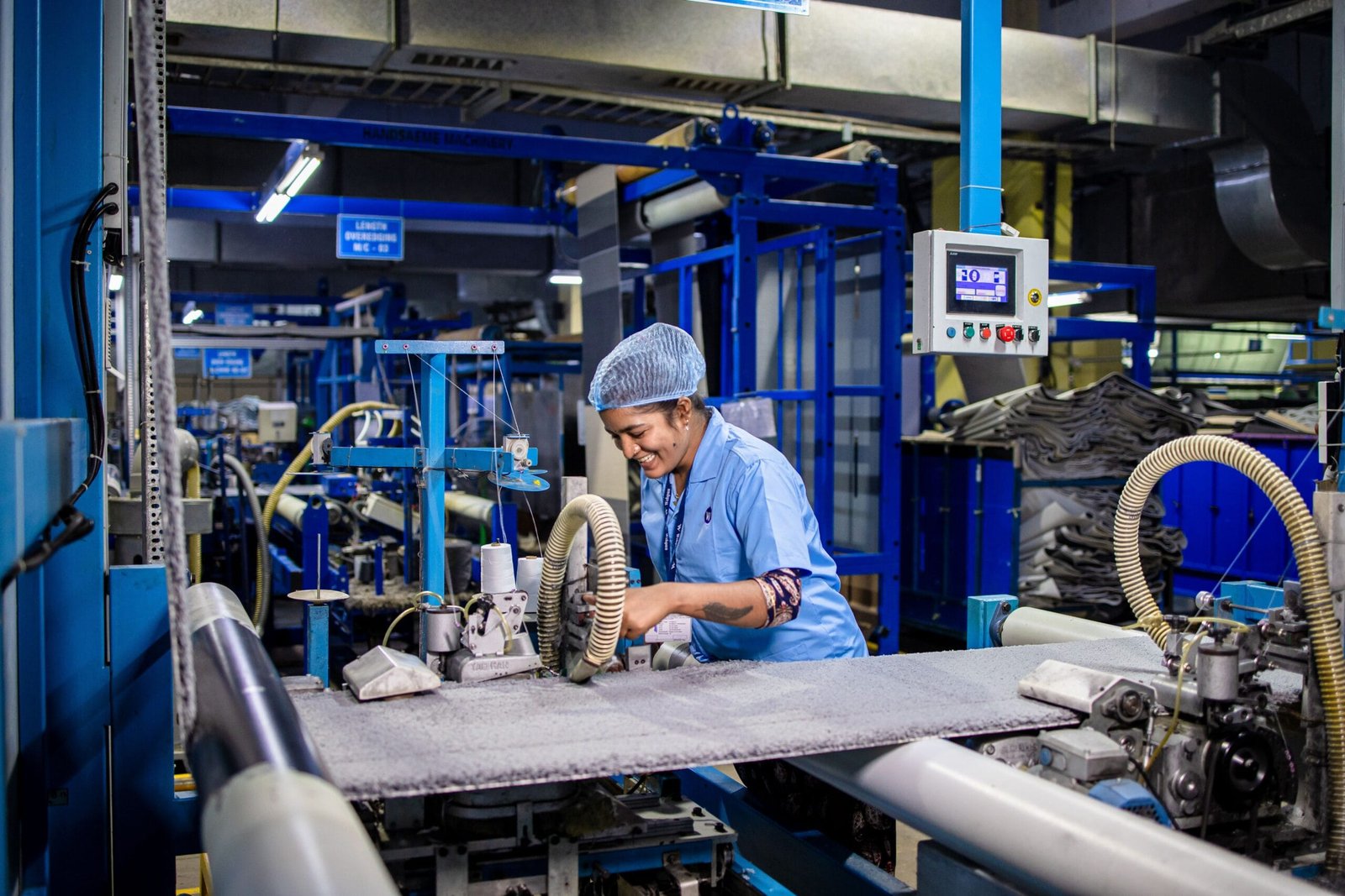 Female factory worker smiling while operating complex textile machinery in an industrial setting