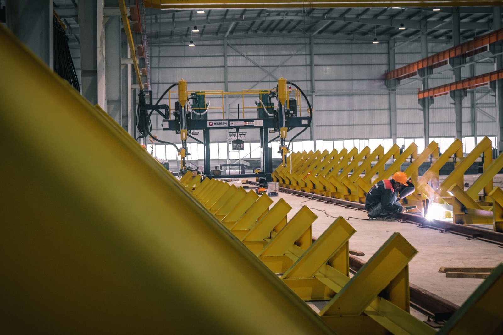 A worker welding metal in an industrial warehouse with heavy machinery