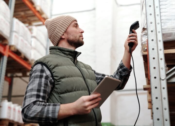 Male warehouse staff scanning inventory with handheld scanner and tablet indoors