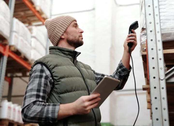 Male warehouse staff scanning inventory with handheld scanner and tablet indoors