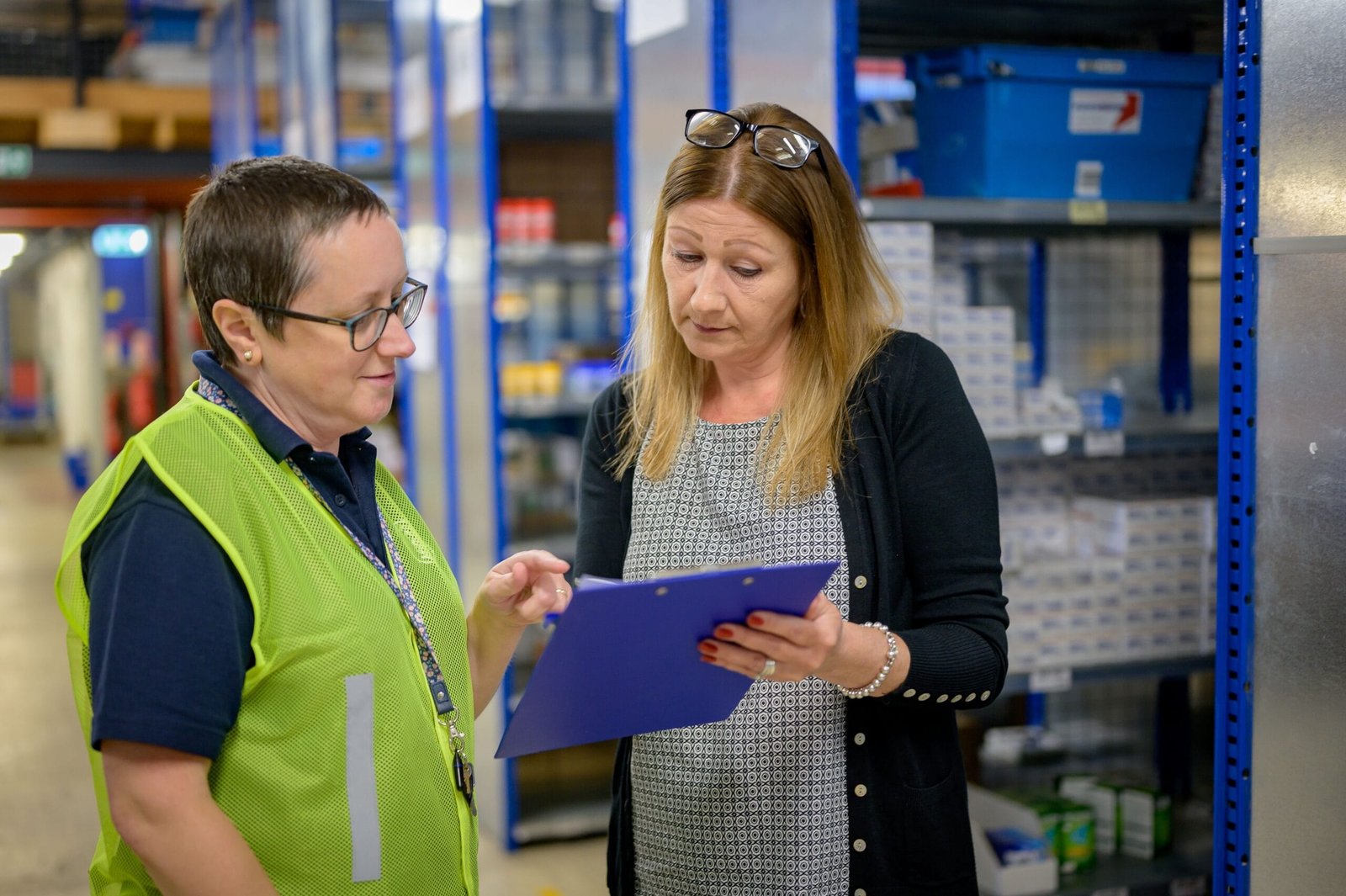 Two women in a warehouse reviewing an inventory checklist on a clipboard