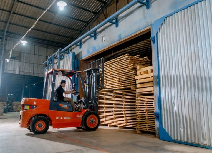 Man operating a forklift indoors loading wooden pallets in a warehouse