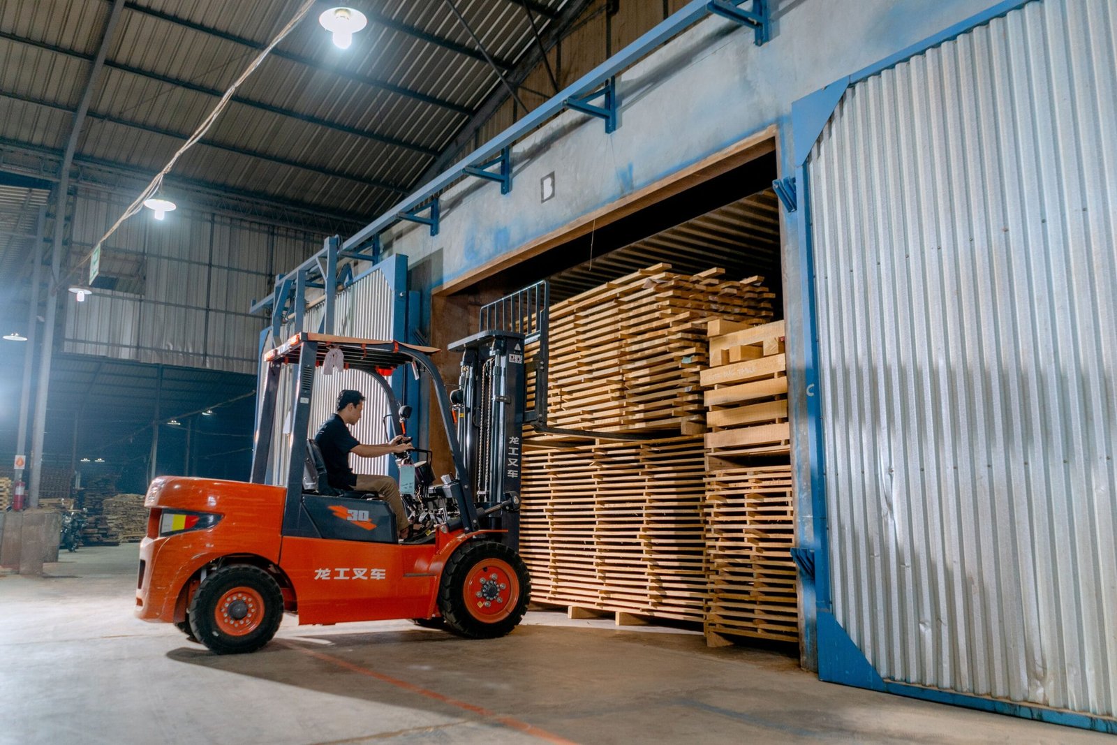 Man operating a forklift indoors loading wooden pallets in a warehouse