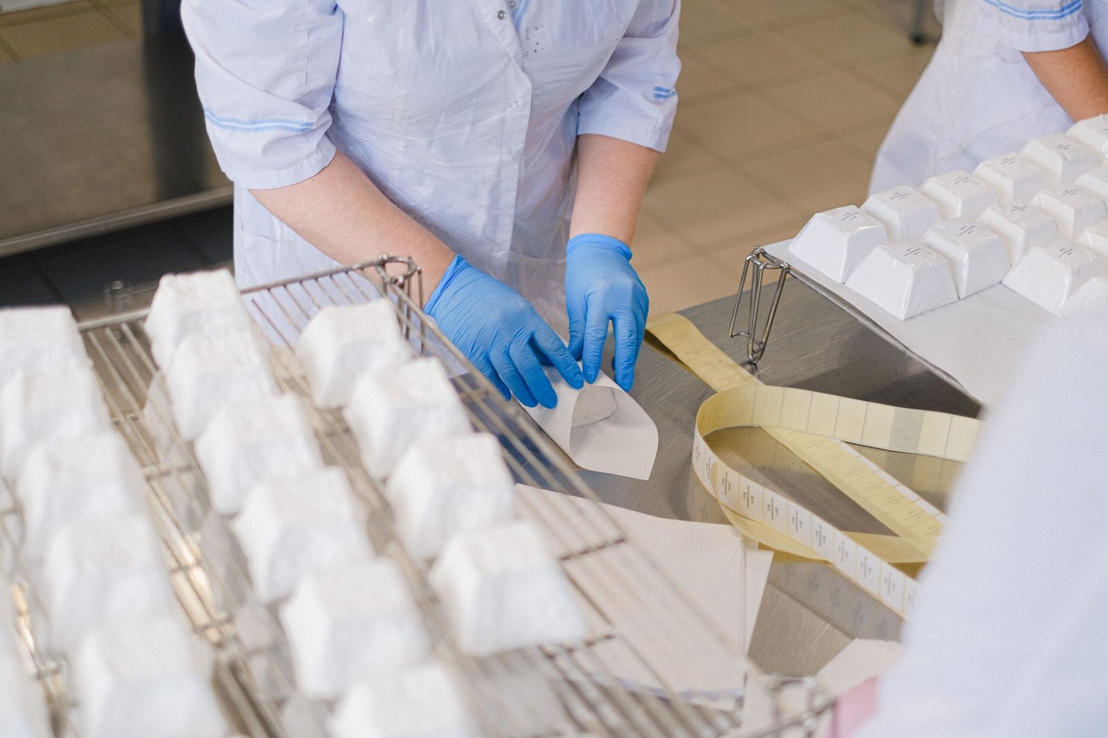 Close-up of hands in blue gloves wrapping cheese blocks in an indoor setting