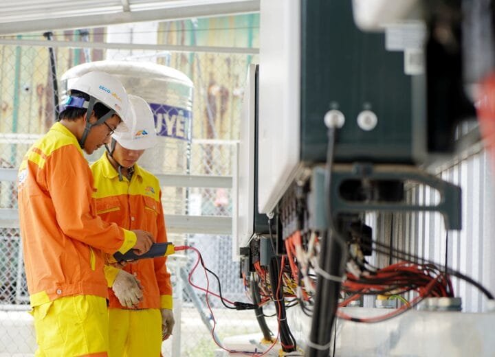 Two technicians with helmets working on electrical equipment outdoors, ensuring safety.