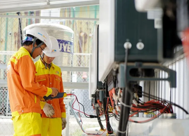 Two technicians with helmets working on electrical equipment outdoors, ensuring safety.