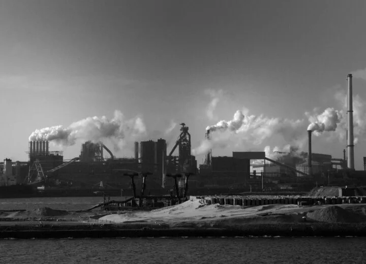 Industrial plant with smokestacks and steam beside water, representing operational efficiency in manufacturing