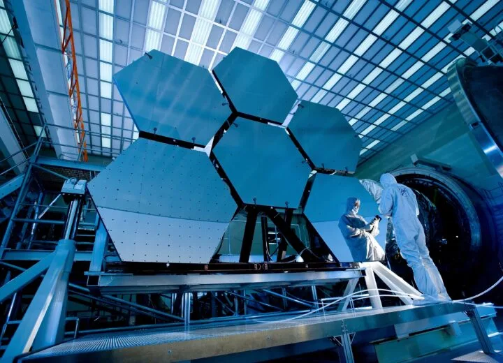 Technicians in white cleanroom suits beside large hexagonal panels, a precision setting for operational efficiency in manufacturing