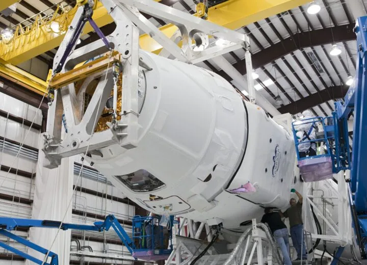 Operational efficiency in manufacturing: workers on lift platforms assembling a large white capsule-shaped structure in a factory